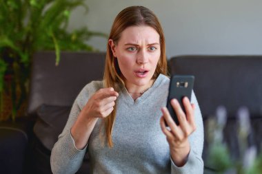 Kanepede dizüstü bilgisayarıyla oturan ve evde telefonla konuşan mutlu kadın..