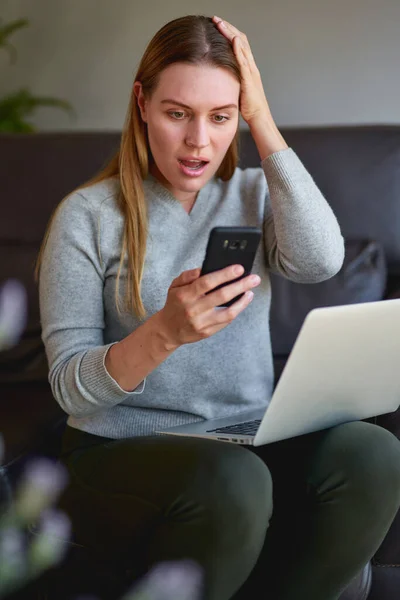 Mujer feliz sentado en el sofá con el ordenador portátil y hablando por teléfono en casa . — Foto de Stock