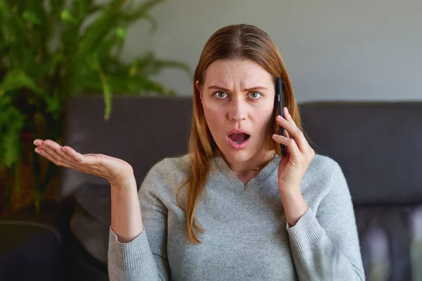 Happy woman sitting on sofa with laptop and talking on phone at home. — Stock Photo, Image