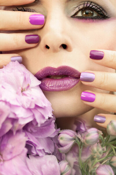 Light pastel multi-colored purple manicure and makeup close - up on a girl with a flower Delphinium.
