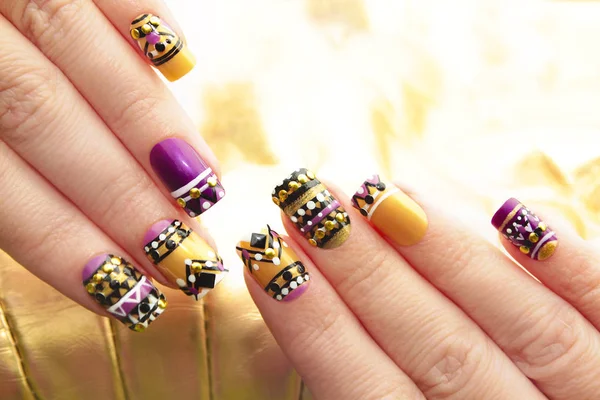 Manicure with colorful ethnic design with rhinestones on female hand close up on colorful background.