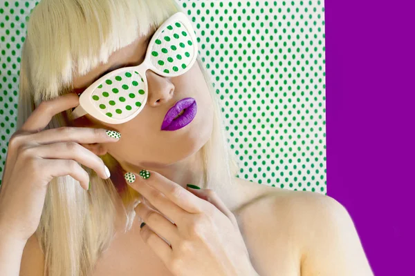 Fashionable coloring hair on light hair with bangs and glasses on the eyes.Nail design and makeup with green dots on model on background with dots.