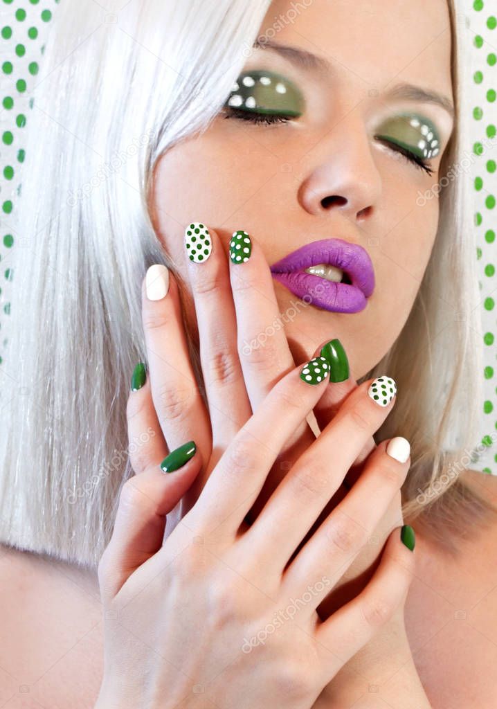Nail design and makeup with green dots on model on background with dots.