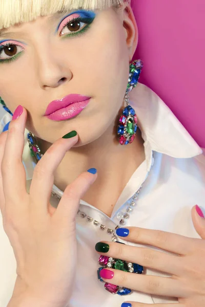 Fashionable colorful short nail art design on female hand close up with decoration on the face.Blue green pink nail Polish.On-trend manicure.