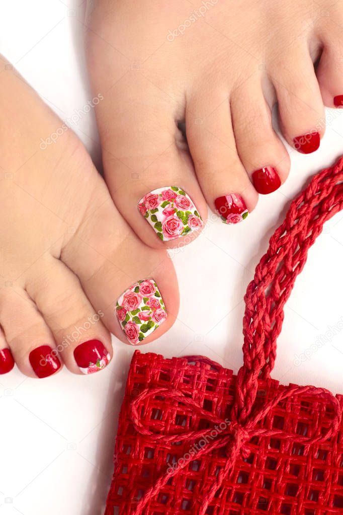 Trendy red summer spring pedicure on the female leg close-up on a white background. Nail Design with roses.