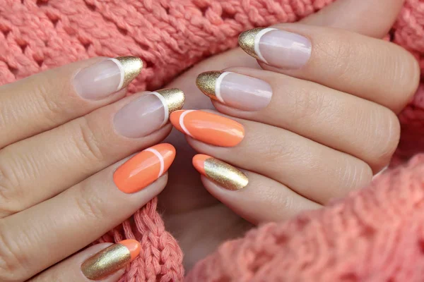 Colorful nail design with peach and golden nail polish. French manicure on a knitted orange background.Colorful nail design with peach and golden nail polish. French manicure on a knitted orange background.