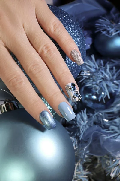 Christmas winter nail design with different colors and patterns of nail Polish with rhinestones.Festive nail art in blue shades.