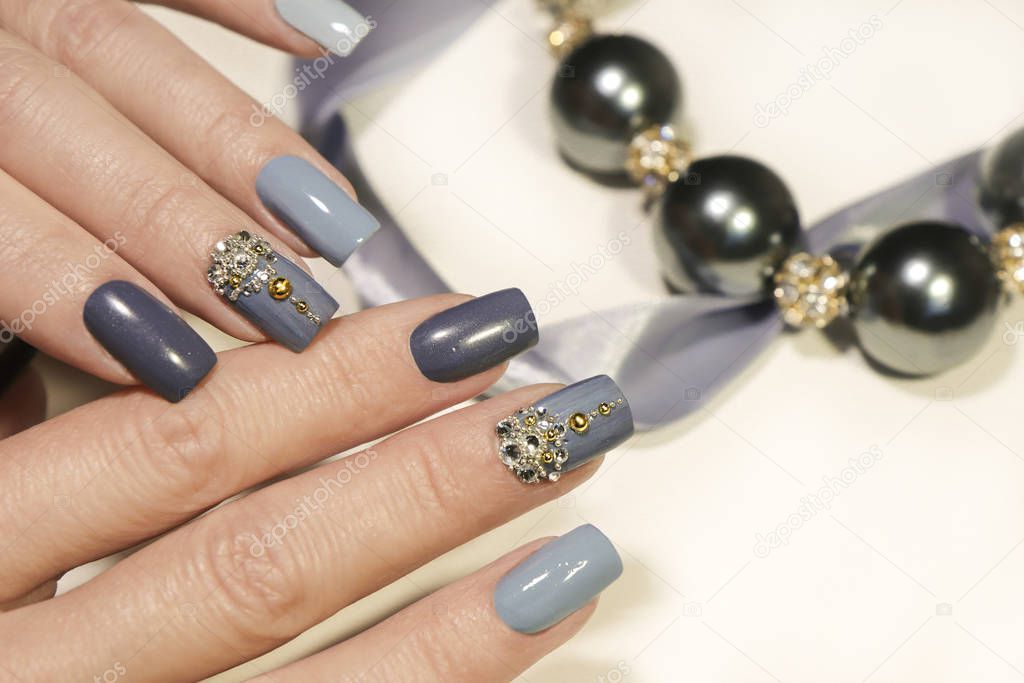 Fashionable grey blue manicure on square shaped nails.Nail art with rhinestones on a light background with decoration.