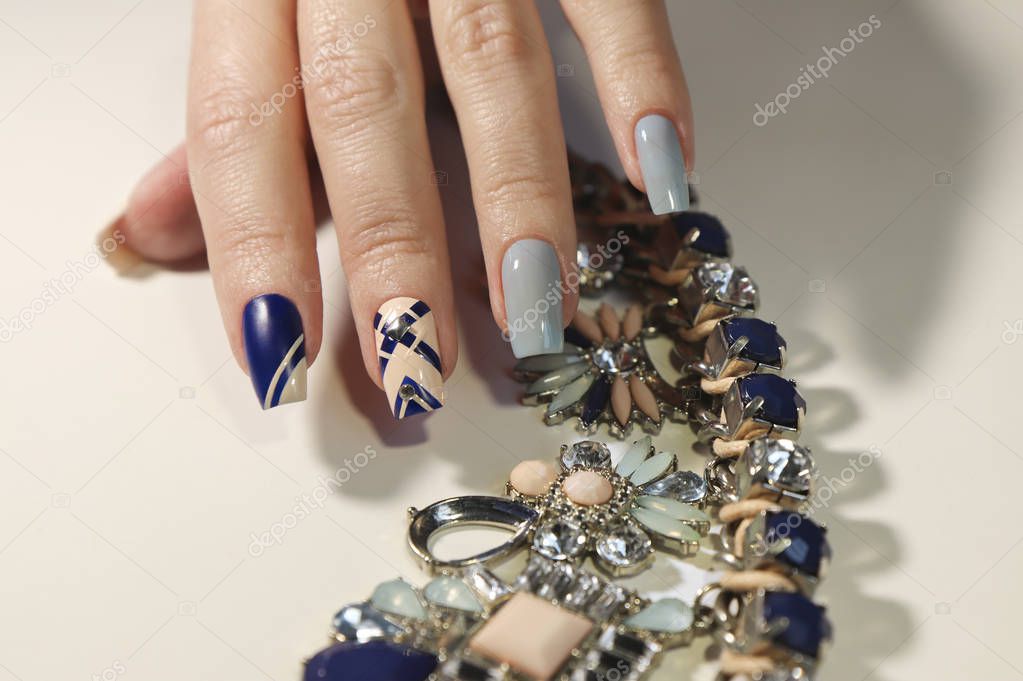 Graphic nail design on beige, transparent blue and dark matte blue nail Polish with metallic rhinestones.Fashionable manicure on a square shape of nails.