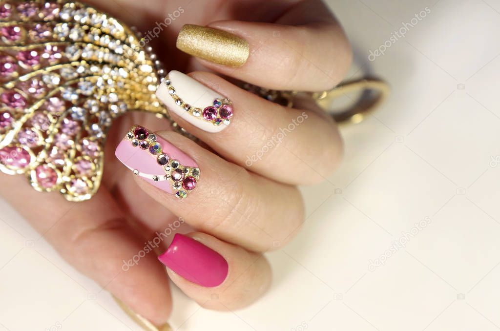 A luxurious manicure with a pink matte finish for nails and a gradient from white with gold to pink nail Polish.Nail art with various shaped rhinestones and colors.