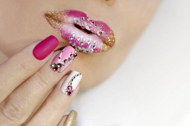 Creative lip makeup and trendy nail art manicure with rhinestones.Matte nail design with a gradient of white, pink and gold nail Polish. clipart