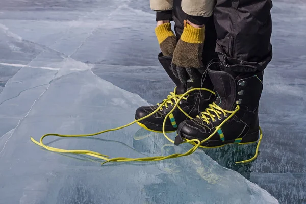 Man is lacing snowboarding bright shoes on the ice with his knitted gloves. — Stock Photo, Image