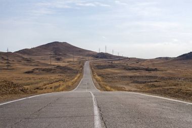 Açık gökyüzü ve kuru ot dağlarla Deniz Baykal için boş eğri kırık asfalt yol arasındadır.