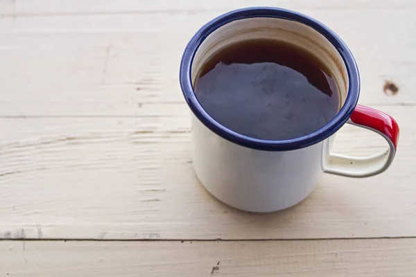 Enameled camping mug with string tea on a wooden texture.