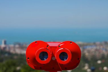 The red coin operated binoculars on the panoramic view of the city Batumi from rooftop platform on the Black Sea with blue sky background. clipart