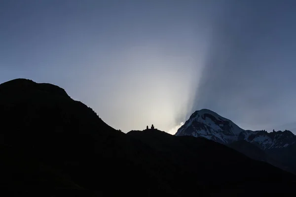 Igreja da Santíssima Trindade na montanha à noite durante o pôr do sol sobre o Monte Kazbek, na Geórgia . — Fotografia de Stock