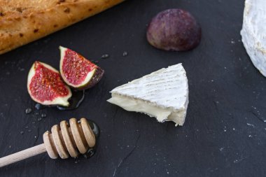 Üçgen iştah açıcı parçası camembert peyniri ve bal ve bir tahta kaşık ve baget grafit arka plan üzerinde incir parçaları.