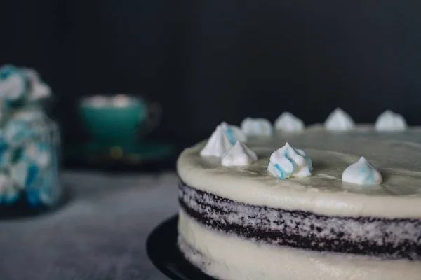 Huisgemaakte chocoladetaart met slagroom versierd met Franse schuimgebak en een mok op een donkere achtergrond. — Stockfoto