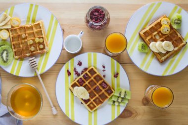 Lezzetli ve besleyici kahvaltıda taze pişmiş Belçika gofret meyve, muz, kivi, Kamkat ve kızılcık, tatlım, gözlük ve bir bardak meyve suyu ile gelen espresso kahve ahşap arka plan üzerinde.