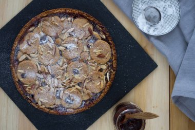 Üstten Görünüm bir bademli kek ahududu ile reçel siyah grafit tepside, bir reçel ve bir tahta kaşık, ahşap mutfak masasında pudra şekeri ile bir daire ile bir cam kavanoz.