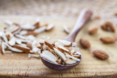 Ahşap oyun tahtası ve ahşap meşe kaşıkla rattan masa üzerinde tüm ve kıyılmış badem fındık.