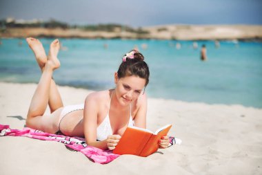 Deniz kıyısında kitap okuyan genç bir kadın.