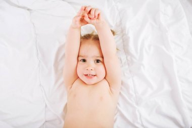 Evde yatakta yatarken ve germe küçük çocuk. 2 yıl eski bebek beyaz battaniye var aittir..