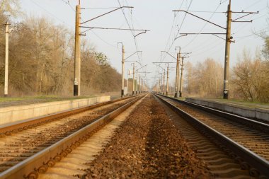 İki tren yolcu, üstünde belgili tanımlık etraf iniş platformları ile elektrik telleri için görünür sütunlar destekler izleri
