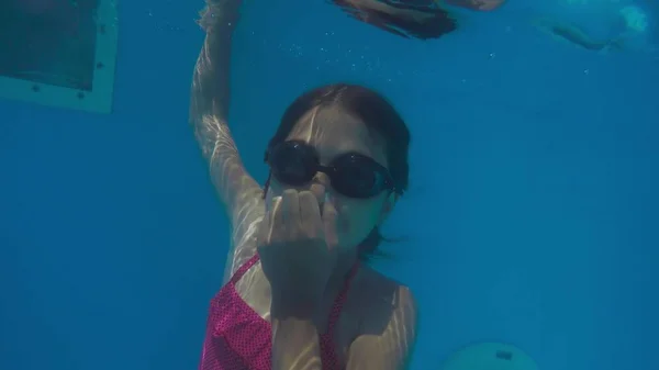 Маленькая девочка в аквапарке плавает под водой и улыбается — стоковое фото