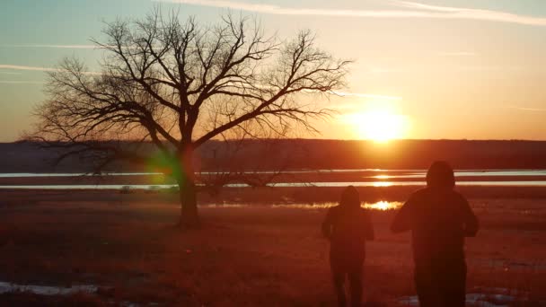 Silhouette two men on the road at sunset standing alone tree silhouette.  Athletic young man running