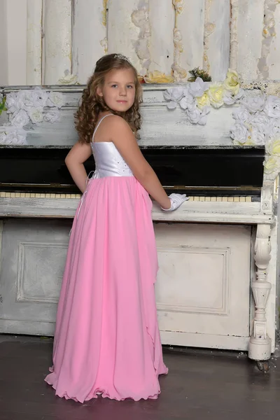 Lány a zongora mellett ünnepi intelligens rózsaszín ruha — Stock Fotó