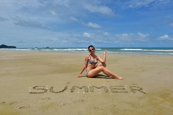 Дівчина в купальнику сидить на пустельному піщаному пляжі поруч з написом літо на піску — стокове фото