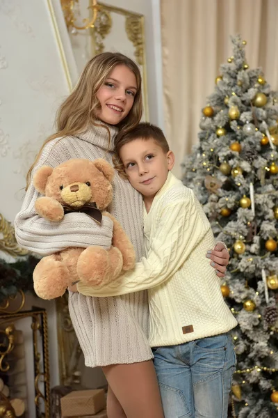 Irmã adolescente e menino com um urso de pelúcia em uma árvore de Natal — Fotografia de Stock