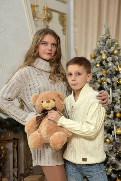 Irmã adolescente e menino com um urso de pelúcia em uma árvore de Natal — Fotografia de Stock