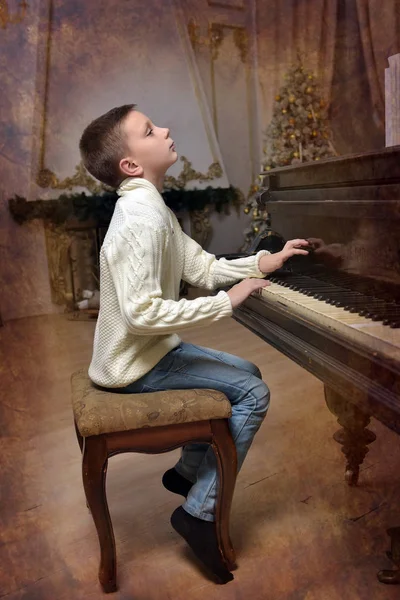 Gutt i hvitt strikket genser ved pianoet – stockfoto