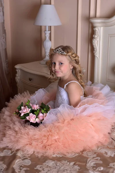 Meisje in het wit met roze jurk en in een diadeem op een sofa — Stockfoto