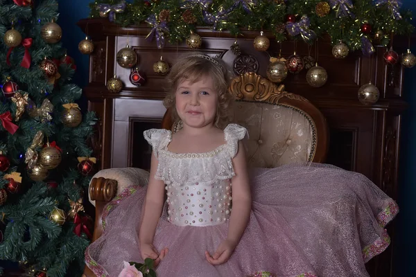 Menina em branco com vestido rosa sentado na cadeira perto de Natal tr — Fotografia de Stock