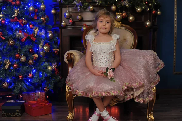 Meisje in het wit met roze jurk zitten in de stoel in de buurt van Kerstmis tr — Stockfoto