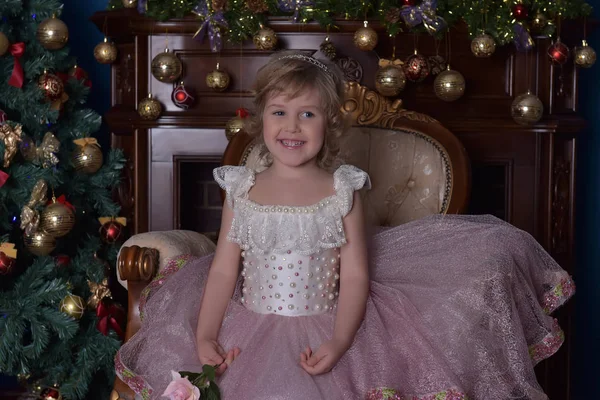 Menina em branco com vestido rosa sentado na cadeira perto de Natal tr — Fotografia de Stock