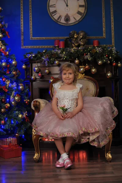 ホワイト クリスマス クリスマス ツリーの近くの椅子に座っているピンクのドレスの女の子 — ストック写真