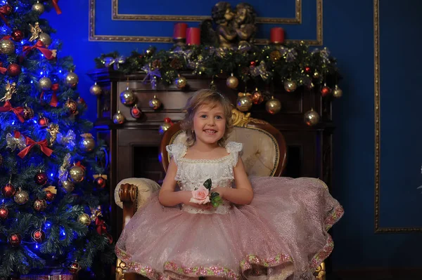 圣诞节时在圣诞树旁坐在椅子上的穿着粉红色衣服的女孩 — 图库照片
