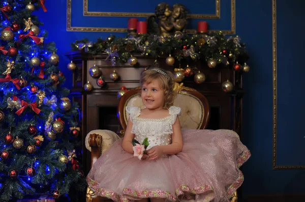 ホワイト クリスマス クリスマス ツリーの近くの椅子に座っているピンクのドレスの女の子 — ストック写真