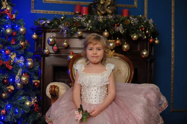 圣诞节时在圣诞树旁坐在椅子上的穿着粉红色衣服的女孩 — 图库照片