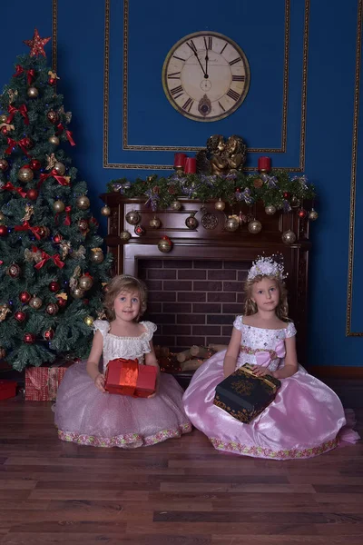 クリスマスに手に贈り物を持って座っているピンクのドレスを着た白い2人の姉妹 — ストック写真