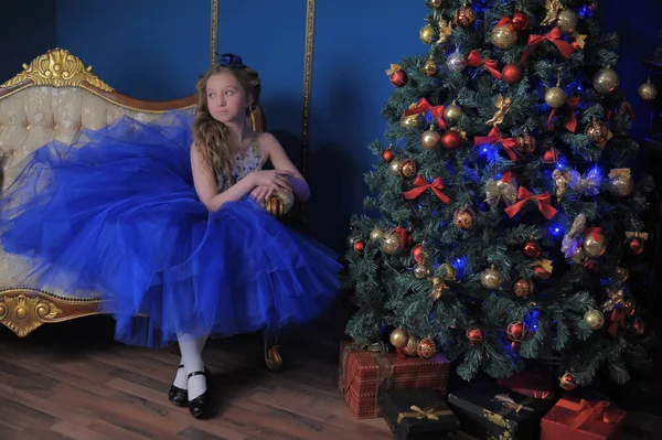 Chica en un vestido azul sentado en el árbol de Navidad — Foto de Stock