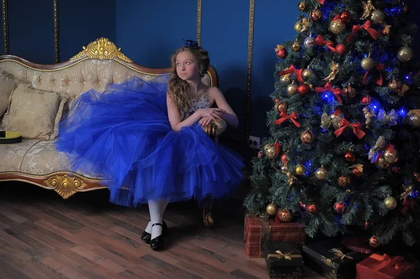 穿着蓝色连衣裙的女孩坐在圣诞树上 — 图库照片