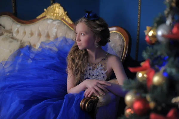 Chica en un vestido azul sentado en el árbol de Navidad — Foto de Stock