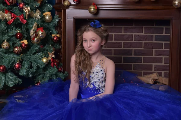 Meisje in blauwe jurk zit bij open haard bij Kerstmis — Stockfoto