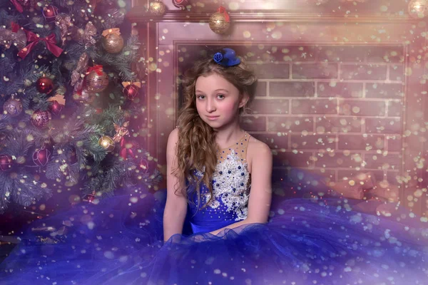 Menina em vestido azul senta-se à lareira na época do Natal — Fotografia de Stock