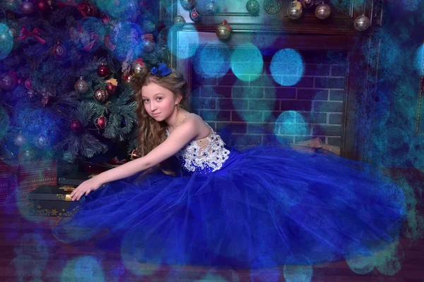 Meisje in blauwe jurk zit bij open haard bij Kerstmis — Stockfoto